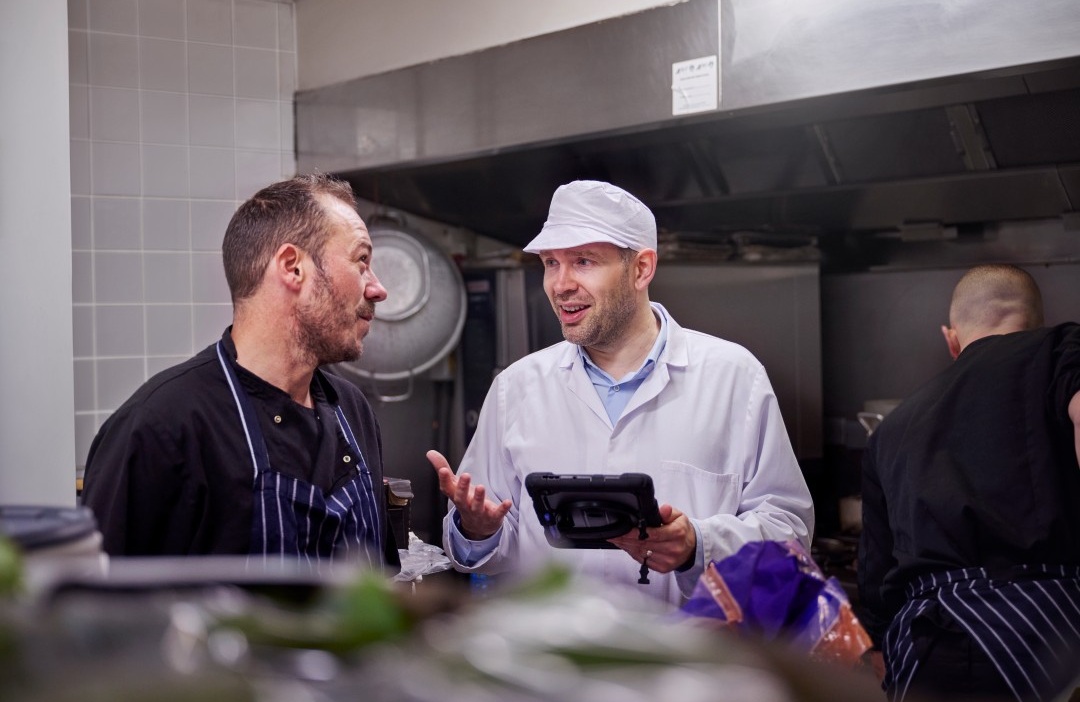 Daniel working in environmental health speaking to a chef in a restaurant kitchen